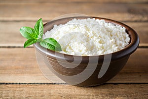 Cottage cheese and mint in ceramic bowl on rustic wooden table