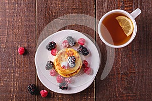 Cottage cheese pancakes, curd fritters dessert with raspberry and blackberry berries in plate near to hot tea cup with lemon slice