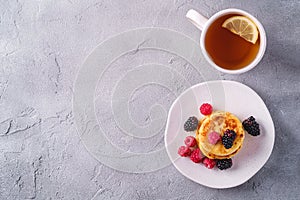 Cottage cheese pancakes, curd fritters dessert with raspberry and blackberry berries in plate near to hot tea cup with lemon slice