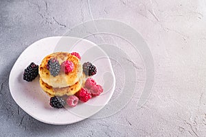 Cottage cheese pancakes, curd fritters dessert with raspberry and blackberry berries in plate on stone concrete background