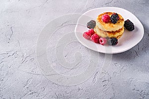 Cottage cheese pancakes, curd fritters dessert with raspberry and blackberry berries in plate on stone concrete background