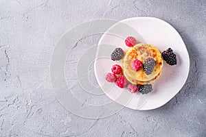 Cottage cheese pancakes, curd fritters dessert with raspberry and blackberry berries in plate on stone concrete background