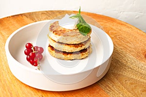 Cottage cheese pancakes or curd fritters stack with sour cream, mint leaf and red currant in white plate