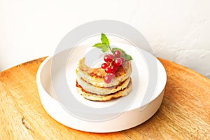 Cottage cheese pancakes or curd fritters stack with sour cream, mint leaf and red currant in white plate
