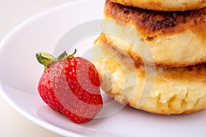 Cottage cheese pancakes with one strawberry on white plate isolated