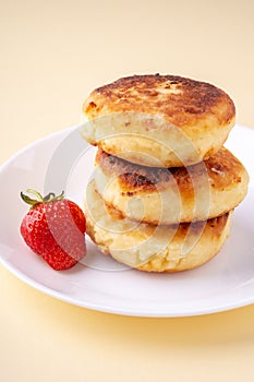 Cottage cheese pancakes with one strawberry on white plate on yellow background isolated