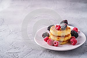 Cottage cheese pancakes and powdered sugar, curd fritters dessert with raspberry and blackberry berries in plate on stone concrete
