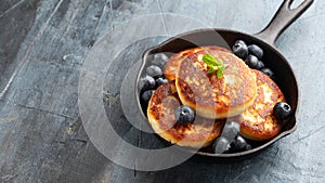 Cottage cheese pancakes served in cast iron frying pan with blueberries and mint leaves. Healthy breakfast food.