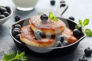 Cottage cheese pancakes served in cast iron frying pan with blueberries and mint leaves. Healthy breakfast food.