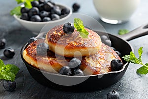 Cottage cheese pancakes served in cast iron frying pan with blueberries and mint leaves. Healthy breakfast food.