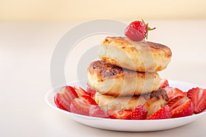 Cottage cheese pancakes with sliced strawberries on white plate isolated