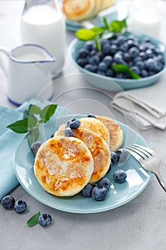 Cottage cheese pancakes, sweet curd fritters with berries, syrniki with honey and fresh blueberry on breakfast table