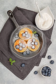 Cottage cheese pancakes, syrniki, curd fritters with fresh berries blueberry,  powdered sugar and sour cream in a cast iron pan