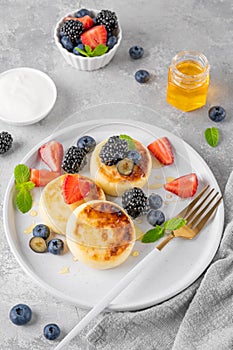 Cottage cheese pancakes, syrniki, ricotta fritters with fresh berries, honey and sour cream on a gray concrete background.