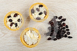 Cottage cheese with raisin and condensed milk in tartlets in plate, dried grape on table. Top view