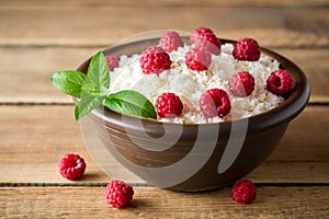 Cottage cheese with raspberry and mint in ceramic bowl on rustic wooden table