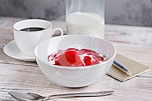 Cottage cheese with sour cream and raspberry jam in a white bowl with coffee and milk on a white wooden table. Healthy breakfast.