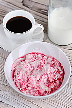 Cottage cheese with sour cream and raspberry jam in a white bowl with coffee and milk on a white wooden table. Healthy breakfast.