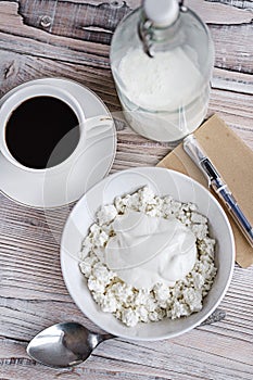 Cottage cheese with sour cream in a white bowl with coffee and milk on a white wooden table. Healthy breakfast. Rustic style