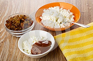 Cottage cheese, spoon, bowl with raisin, bowl with cottage cheese and boiled condensed milk on table