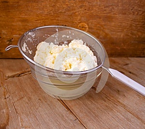Cottage cheese in strainer in bowl with Liquid milk whey on wooden background. Dairy production concept