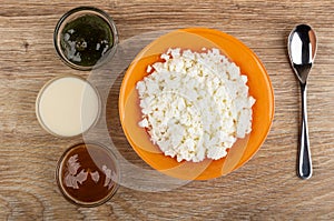 Cottage cheese, teaspoon, bowls with gooseberry jam, condensed milk, boiled condensed milk on table. Top view