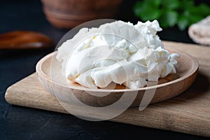Cottage cheese on a wooden stand. Cottage cheese in a bowl. Soft cheese and wooden spoon on a wooden boards