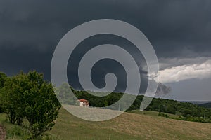 A cottage with a green forest in the background and a stormy sky