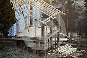 Cottage house building under construction with walls made of hollow foam insulation blocks, wooden roof frame and attached porch