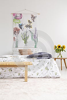 Cottage house minimal bedroom interior with colorful flowers and birds painted on fabric above a bed which is dressed in natural t