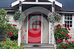 Cottage red door with geraniums and other flower baskets on front porch photo