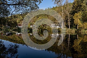 Cottages and small houses among the trees reflected on the surface of the river Sazava