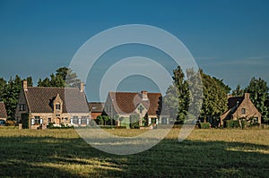 Cottages and trees in front of cultivated fields at the late afternoon light, next the village of Damme.