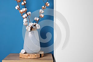 Cotton branches with fluffy flowers in vase on wooden table indoors. Space for text