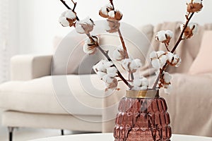 Cotton branches with fluffy flowers on white table in cozy room. Space for text