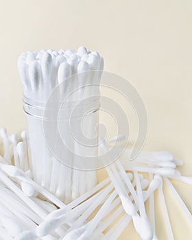 Cotton buds are placed in a container, surrounded by cotton buds on a beige background.