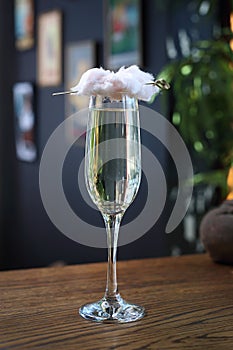 Cotton candy champagne cocktail. Prosecco in a tall flute glass served with a cotton candy cloud, on a wooden table.