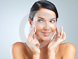 Cotton pad, beauty and woman cleaning makeup from face, dermatology and skincare with facial on grey background