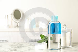 Cotton pads, leaves and makeup removal product on white marble table in bathroom. Space for text photo