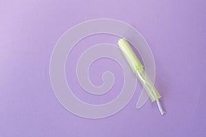 Cotton tampon with light green opened applicartor on violet background. Woman days hygiene protection. Menstrual cycle period