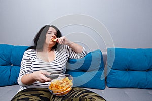 Couch potato overweight woman sitting on the sofa, eating chips