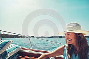 She couldnt be happier. an attractive young woman sitting at the back of a yacht on the open seas.