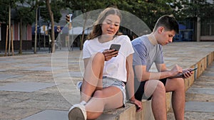 A coulpe of teenagers with smartphones is sitting on the step