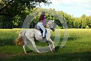 Counrty girl riding horseback on a meadow against woods