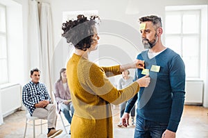 Counselor putting adhesive notes with the word sad on client during group therapy.