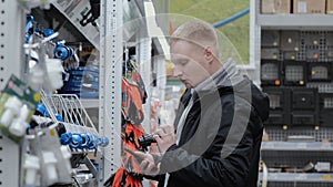 Counter with household goods. Young man in a hardware store. A man in a store chooses accessories for watering the lawn