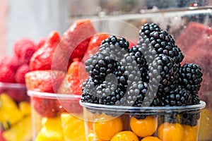 Counter with plastic containers and cups filled of fresh berries. Blackberry, strawberry, blueberry