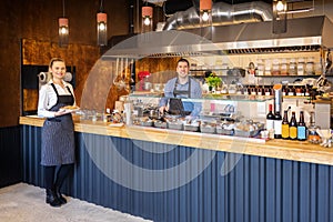 Counter service at modern bistro with smiling waiters serving food Ã¢â¬â happy business owners in small restaurant with open kitchen