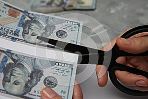 Counterfeiter cutting dollar banknotes with scissors at grey marble table, closeup. Fake money photo