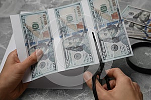 Counterfeiter cutting dollar banknotes with scissors at grey marble table, closeup. Fake money photo